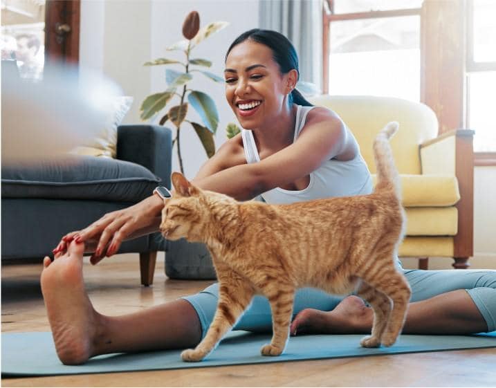 Mujer haciendo yoga mientras un gato se acurruca